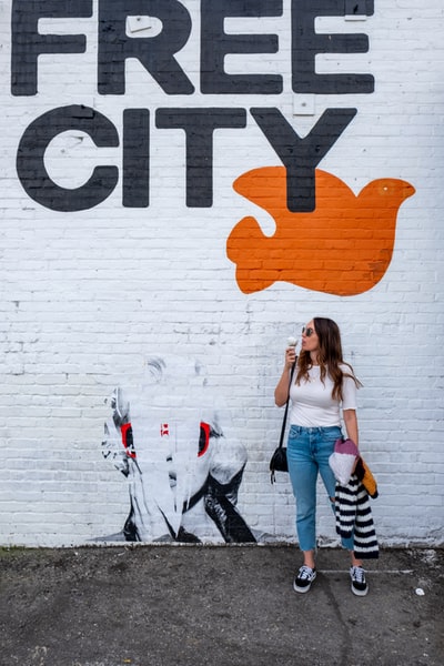 女子站在墙旁边拿着冰淇淋和免费的城市标志

